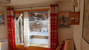Une pièce chaleureuse avec un plancher en bois, un canapé rouge, une table avec une lampe et une fenêtre ornée de rideaux rouges.