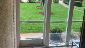 A room with a view of a well-maintained lawn and a white building in the background. - Lely Resort Golf Community beautiful condo. (Naples)