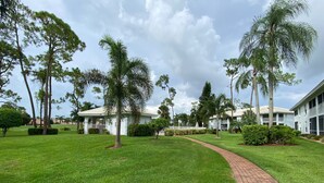 A well-maintained grassy area with a brick pathway leading to a building with a white facade and multiple windows. - Lely Resort Golf Community beautiful condo. (Naples)