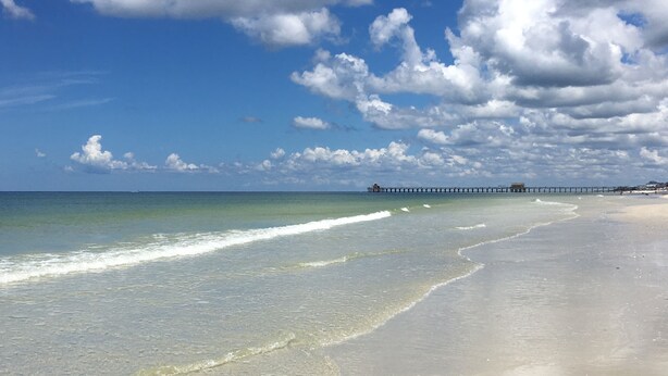A beach with clear water, a sandy shore, and a pier in the distance. - Lely Resort Golf Community beautiful condo. (Naples)