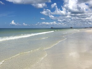 A beach with clear water, a sandy shore, and a pier in the distance. - Lely Resort Golf Community beautiful condo. (Naples)
