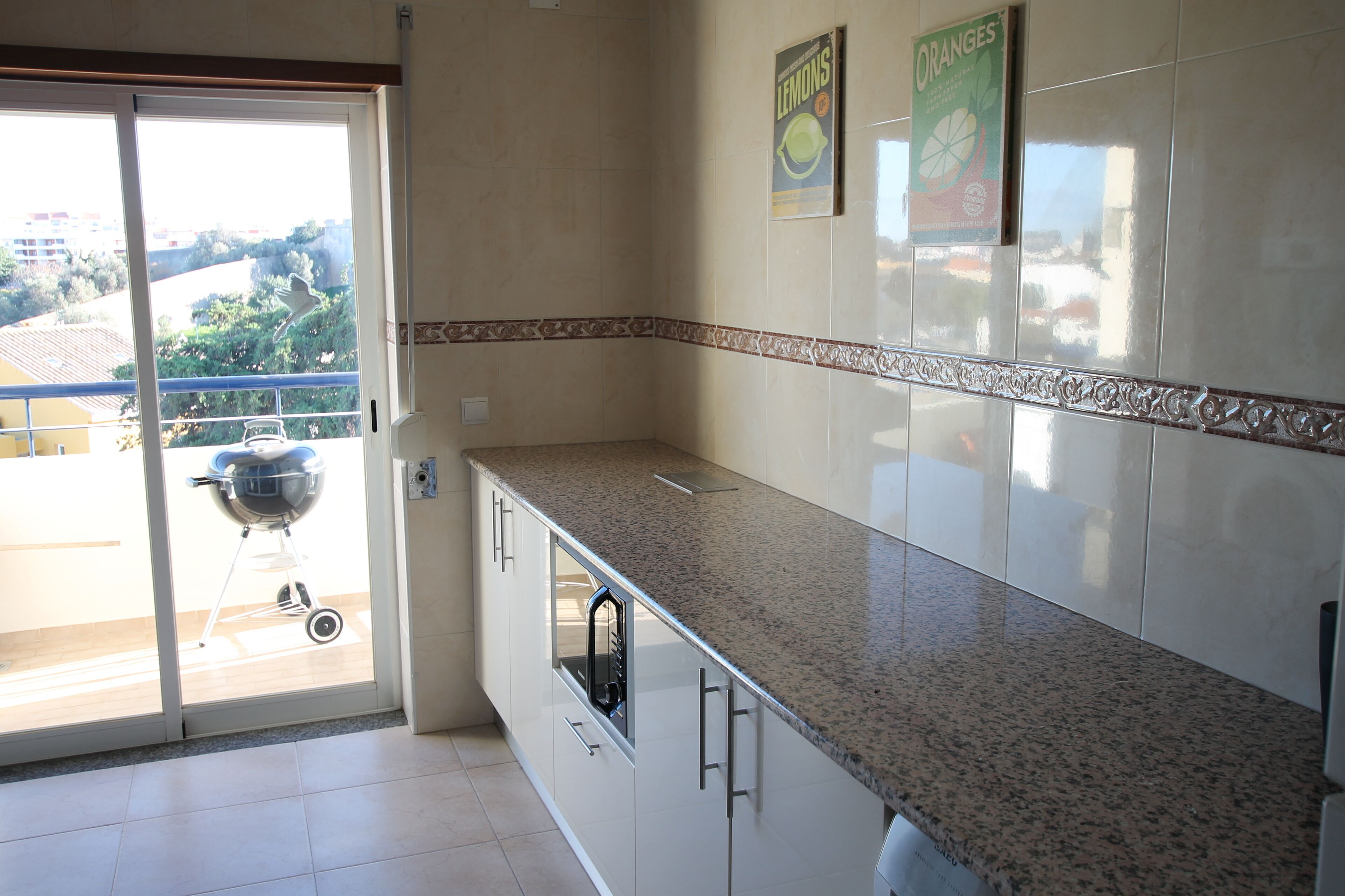 A kitchen with a granite countertop, white cabinets, and a sliding glass door leading to a balcony with a barbecue grill.