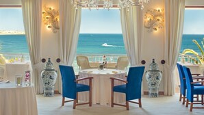 Un espace repas avec vue sur la mer, comprenant une table ronde, des chaises bleues et des vases décoratifs.