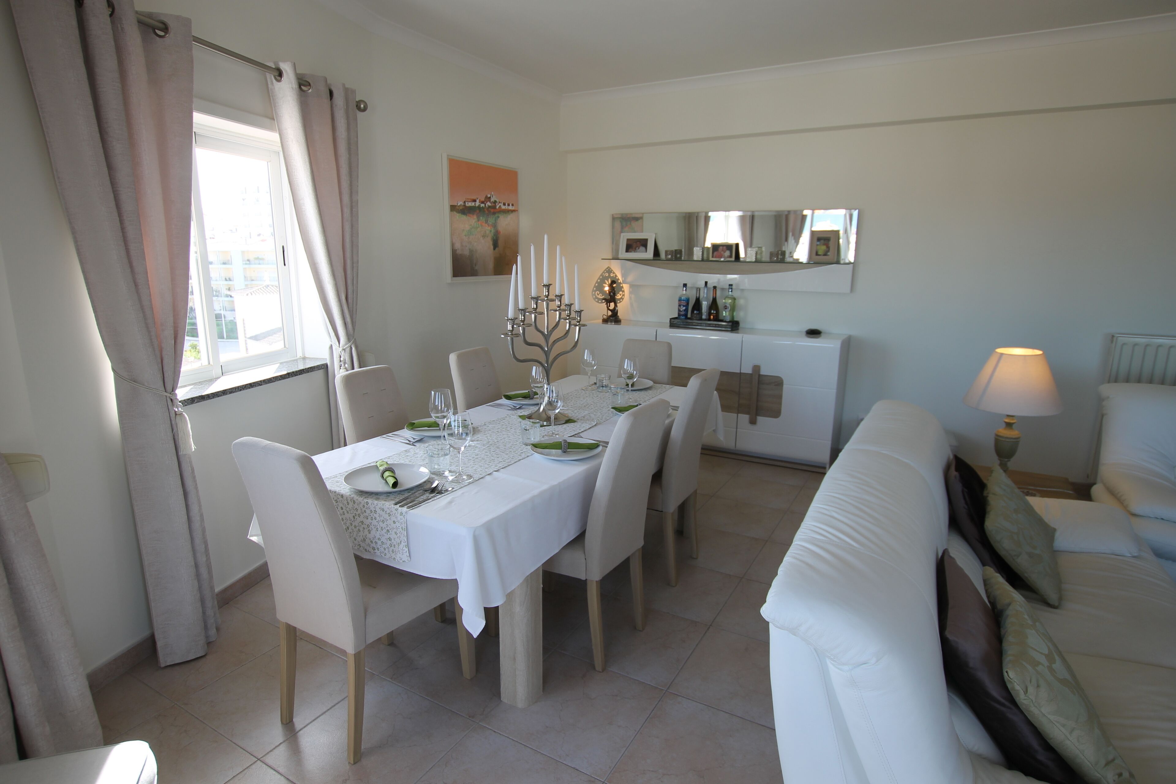 A dining area with a table set for six, a sofa, and a lamp.