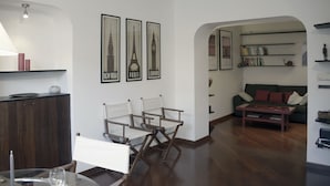 A modern living room with a dining area, featuring a wooden cabinet, a dining table with chairs, a sofa, and a coffee table. There are framed pictures of famous landmarks on the wall. - Delightful two-room apartment in the heart of Genoa. (Genova)