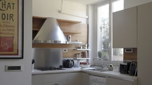A modern kitchen with a built-in stove, a large range hood, a dishwasher, and a window providing natural light. - Delightful two-room apartment in the heart of Genoa. (Genova)