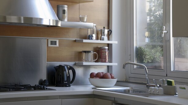 A modern kitchen with a gas stove, a coffee maker, a kettle, and a bowl of fruit. - Delightful two-room apartment in the heart of Genoa. (Genova)