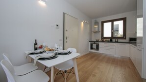 A modern kitchen with white cabinetry, a dining area with a table set for two, and a window with a view of the outdoors. - Argegno Home, Argegno, Italy (Argegno)