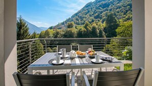 A balcony with a table set for breakfast, overlooking a mountainous landscape. - Argegno Home, Argegno, Italy (Argegno)