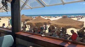 Un restaurant situé en bord de mer, avec une terrasse, des parasols en chaume et une vue sur la plage et l’océan.