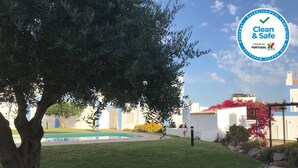 Une cour avec un arbre, une piscine et un bâtiment blanc orné de fleurs rouges.
