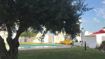A courtyard with a tree, a pool, and a white building with red flowers.