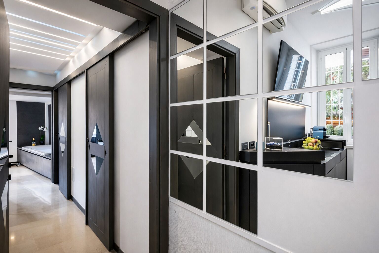 Un couloir d’hôtel moderne avec une cloison en verre, un lavabo orné de fruits et un téléviseur.