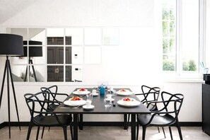 A modern dining area with a table set for four, black chairs, a floor lamp, and a window with a view of greenery.