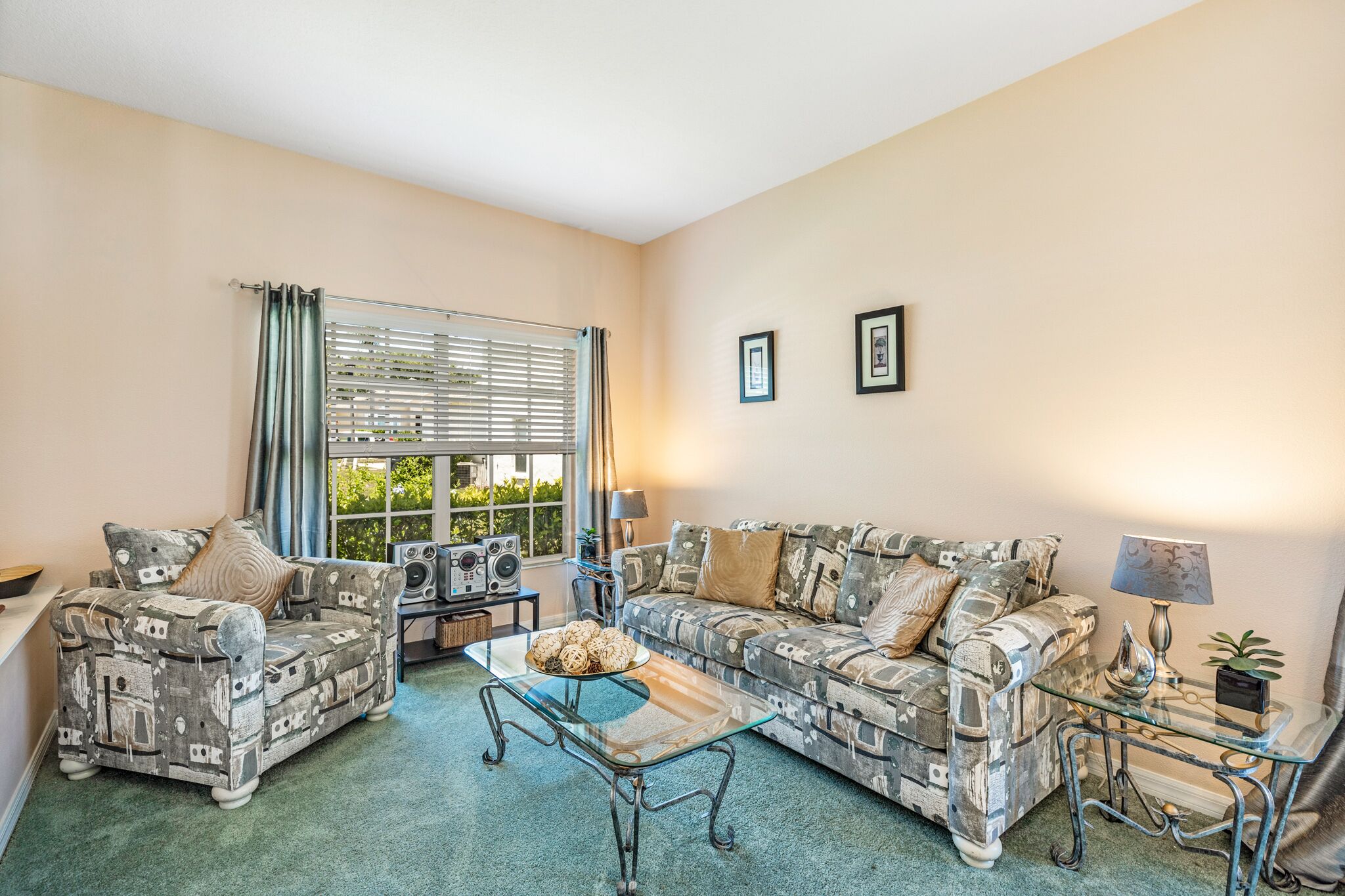 A living room with two patterned sofas, a glass coffee table, and a window with blinds.