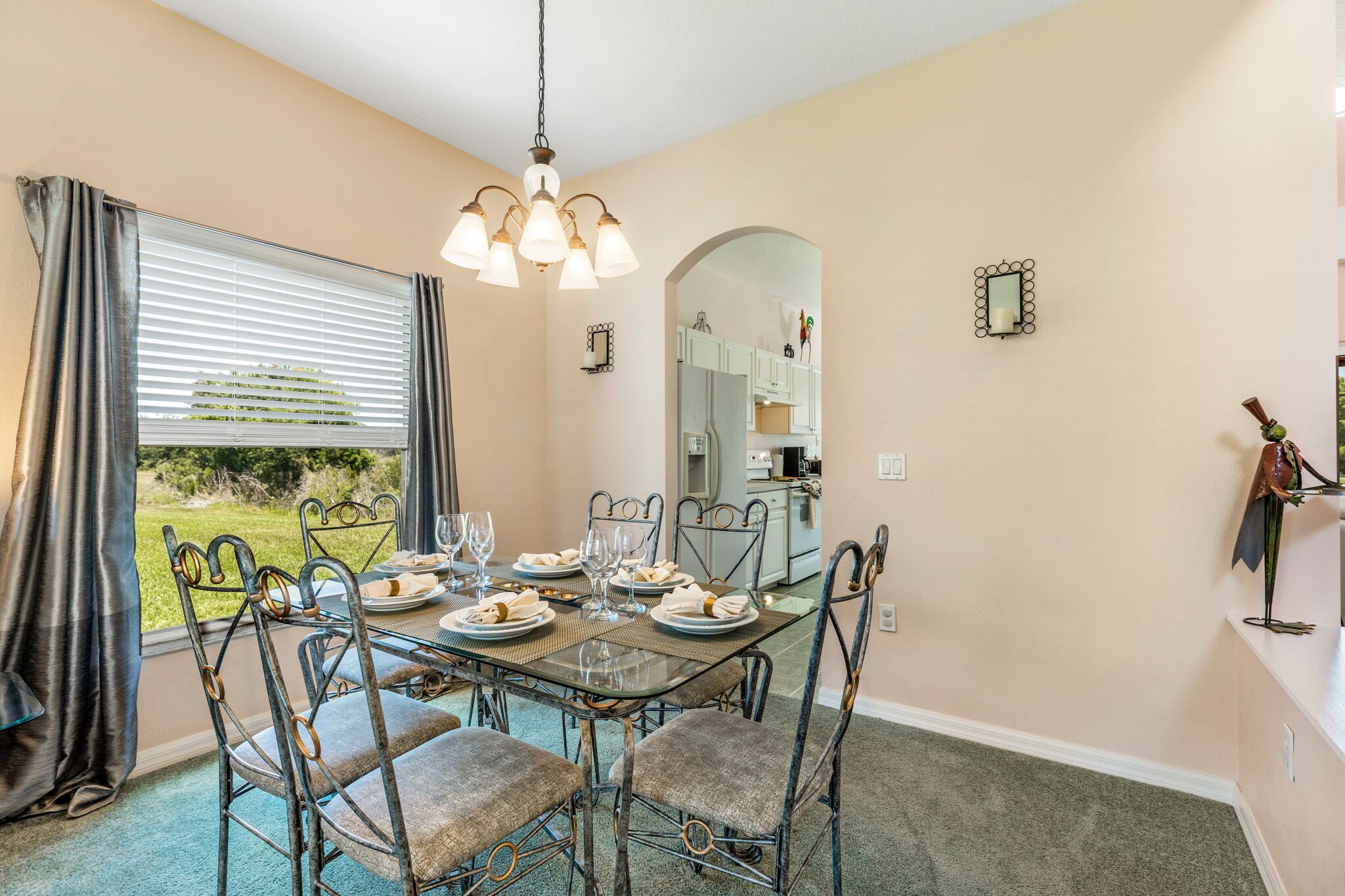 A dining area with a table set for four, a chandelier, and a view of the outdoors.