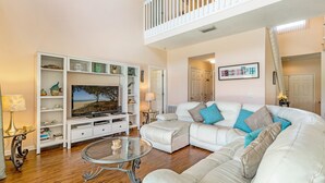 A spacious living room with a white sectional sofa, a glass coffee table, and a white entertainment unit with a flat-screen TV. - Stunning 4 Bed Villa With Uninterupted Lake Views In The Sanctuary  (Davenport)