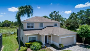 A two-story house with a garage, surrounded by a well-maintained lawn and a small pond. - Stunning 4 Bed Villa With Uninterupted Lake Views In The Sanctuary  (Davenport)