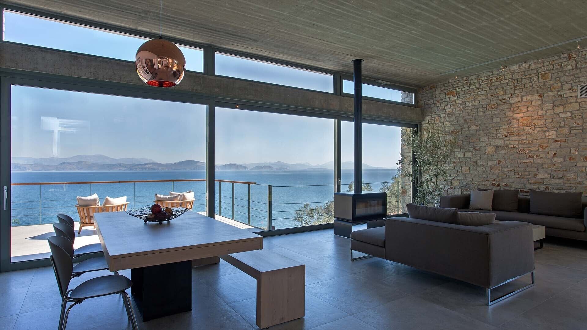 Ein modernes Wohnzimmer mit großem Fenster, das auf ein Gewässer und Berge blickt.