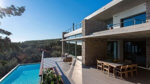 Una casa moderna de dos pisos con piscina, mobiliario exterior y vistas del paisaje circundante.