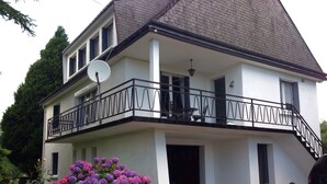 Una casa a due piani con un balcone, un'antenna parabolica e un giardino con ortensie.
