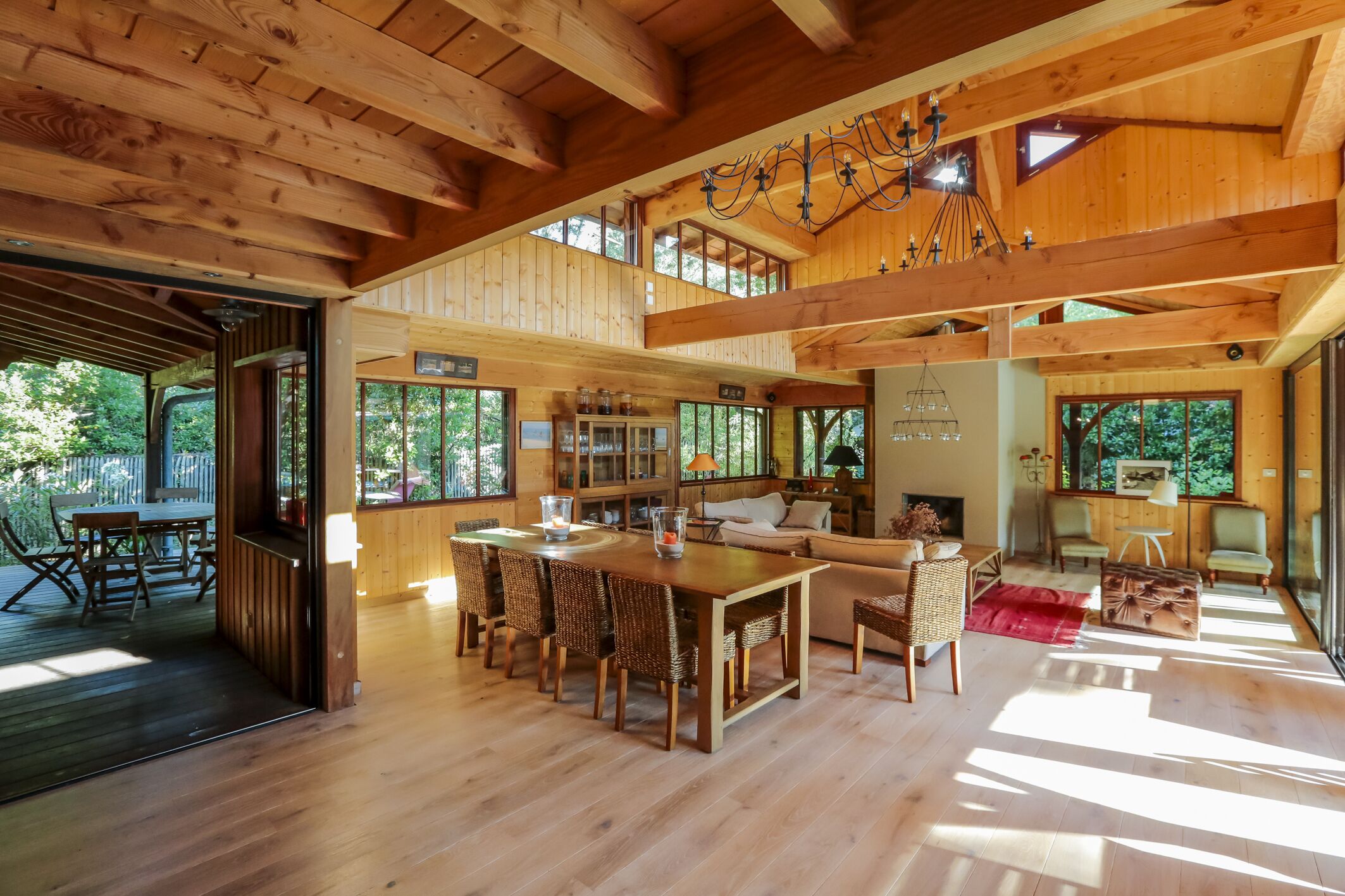 Un intérieur spacieux en bois, avec un plafond haut, un coin repas doté de chaises en osier, un canapé et une cheminée.