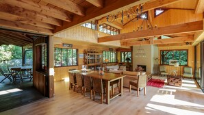 A spacious wooden interior with a high ceiling, a dining area with wicker chairs, a sofa, and a fireplace. - Charming house in Cap Ferret with private pool in a haven of peace (Lège-Cap-Ferret)