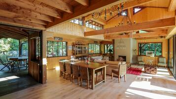 Un intérieur spacieux en bois, avec un plafond haut, un coin repas doté de chaises en osier, un canapé et une cheminée.