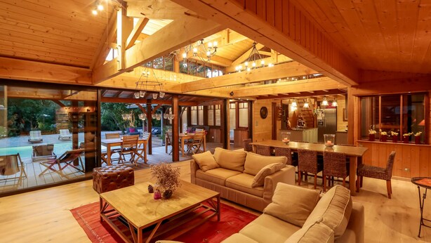 A spacious living area with a high ceiling, wooden beams, and a dining area with a kitchen in the background. - Charming house in Cap Ferret with private pool in a haven of peace (Lège-Cap-Ferret)