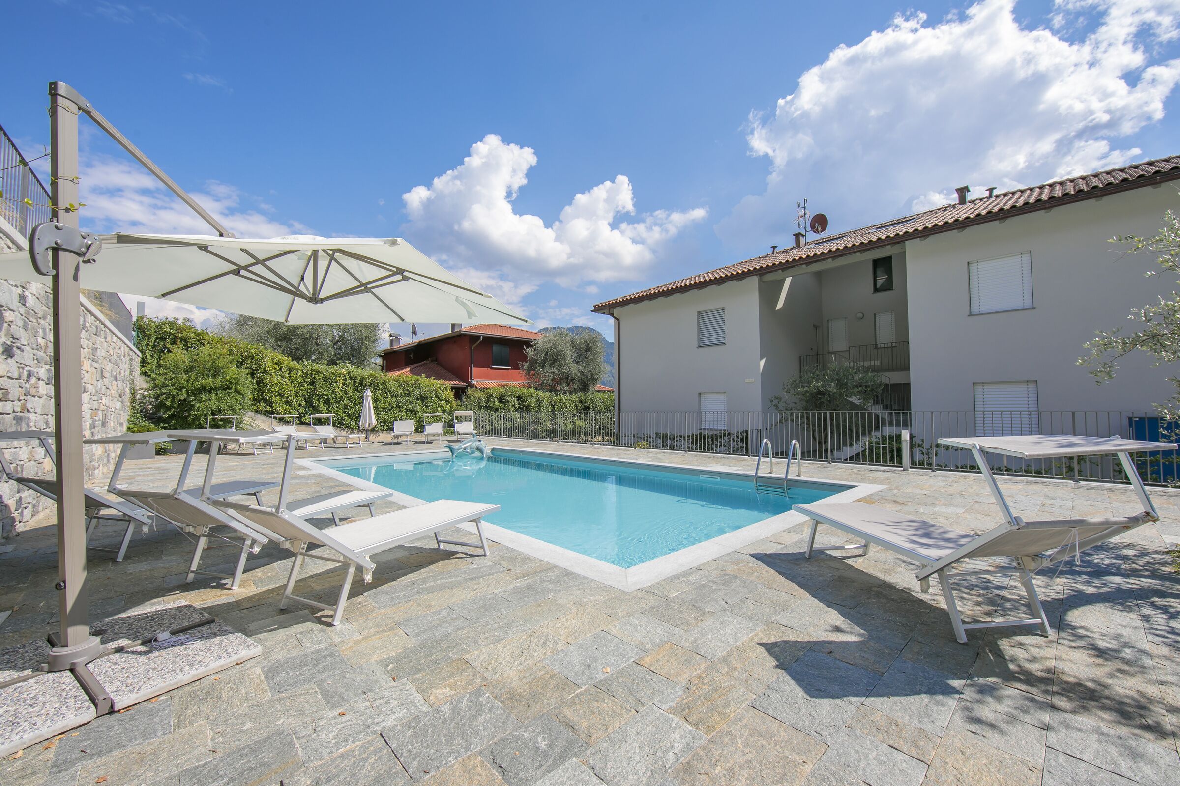 A swimming pool with lounge chairs and umbrellas, surrounded by stone tiles and a stone wall.