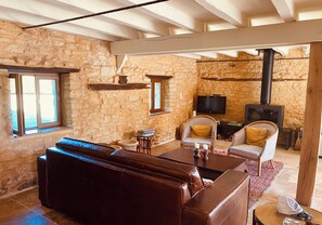Una habitación rústica con paredes de piedra, un sofá de cuero, un televisor y una estufa de leña.