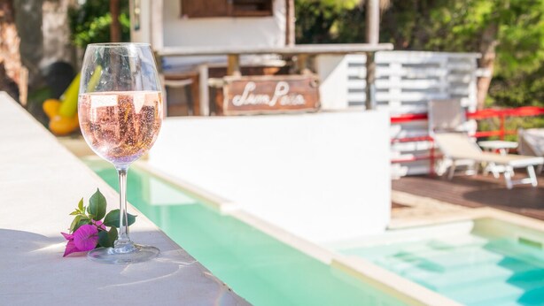 A glass of wine on a poolside table with a pool and lounge chairs in the background. - Splendid Villa with private pool and stunning views in Sperlonga, near Rome (Sperlonga)
