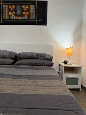 A neatly made bed with a patterned bedspread, a bedside table with a lamp and clock, and a framed artwork above the bed.