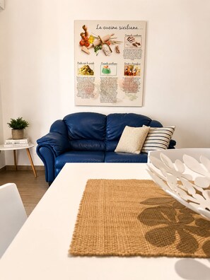 A modern living room with a blue sofa, a white table, and a wall-mounted menu board.