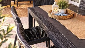A sunlit outdoor seating area with wicker furniture, a potted plant, and decorative wall lights.