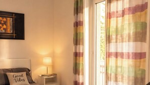 A bedroom with a bed, bedside table, lamp, and a view of the outdoors through a door.