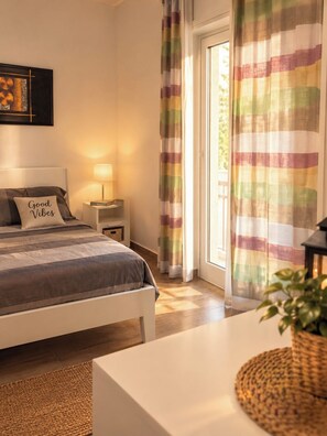 A bedroom with a bed, bedside table, lamp, and a view of the outdoors through a door.
