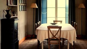 Ein Esszimmer mit Tisch für vier Personen, beleuchtet von zwei Lampen, mit Bücherregal und Fenster mit Vorhängen.