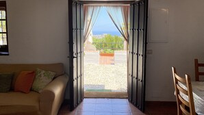 Une porte ouverte donnant sur un balcon avec vue sur la mer et la verdure.