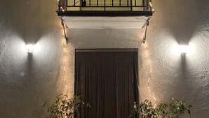 Une entrée d’immeuble avec un luminaire en forme d’étoile au-dessus de la porte, deux plantes en pot de chaque côté et un balcon avec une balustrade.