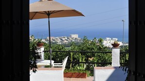 Un balcon avec un parasol beige, des plantes en pot et une vue sur le paysage urbain de la côte.