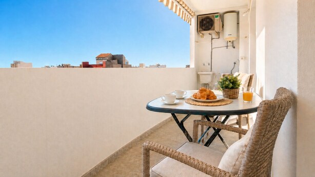 Un balcon avec une table préparée pour le petit-déjeuner, comprenant des croissants, du café et du jus de fruits.