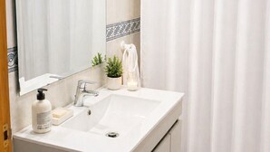 Une salle de bain avec un lavabo blanc, un miroir et un rideau de douche.