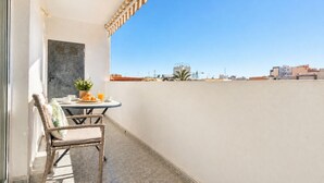 Un balcon avec un fauteuil en osier, une petite table avec une plante et un verre de jus d’orange.