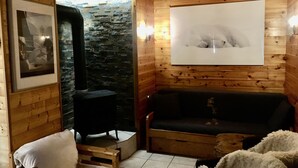 Una habitación acogedora con paredes de madera, una chimenea de piedra, un sofá negro, una silla blanca y un cuadro enmarcado.