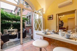 Ein sonnendurchfluteter Essbereich mit Glastür zum Garten, ein mit Geschirr gedeckter weißer Tisch und ein Fliesenboden.