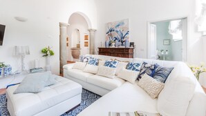 Ein modernes Wohnzimmer mit einem weißen Sofa, dazu passendem Hocker und einer dekorativen Wandgestaltung.