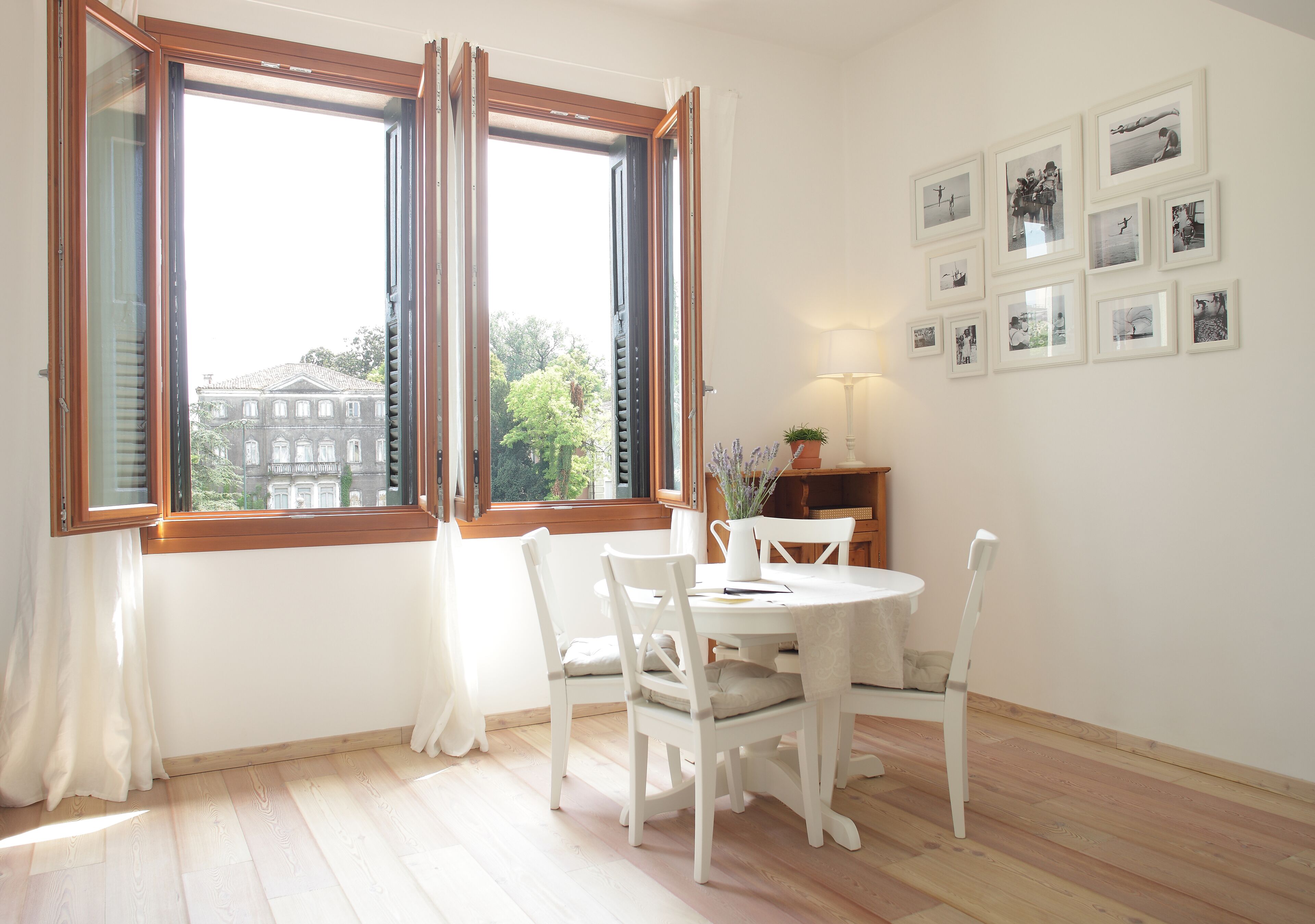 Un comedor con mesa y sillas, una ventana con contraventanas abiertas y una pared con cuadros enmarcados.