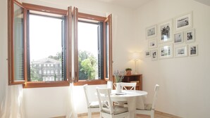 A dining area with a table and chairs, a window with open shutters, and a wall with framed pictures. - THE RIVERSIDE SUITE and POOL near VENICE (Mira)