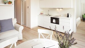 A modern kitchen with white cabinetry, a built-in oven, and a sink. There is a dining area with a white table and chairs, and a vase of lavender flowers. - THE RIVERSIDE SUITE and POOL near VENICE (Mira)